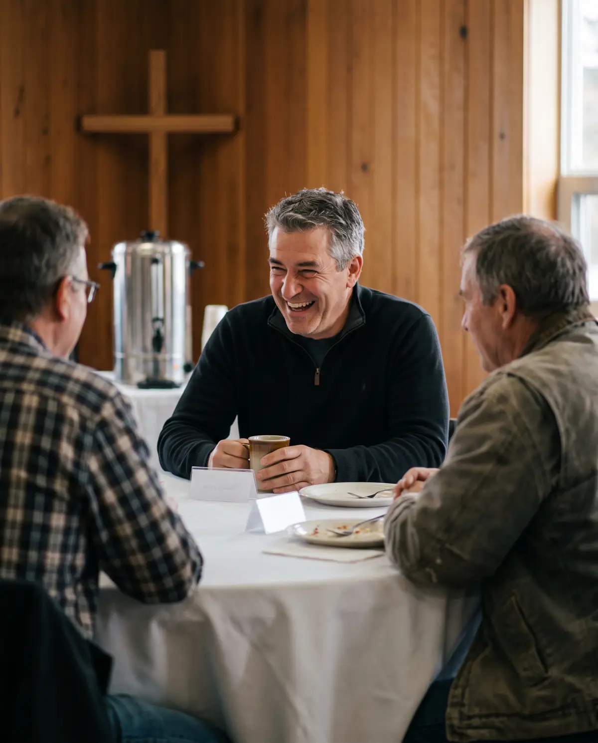 Local business owners laughing over coffee at a Christian business breakfast in a church hall